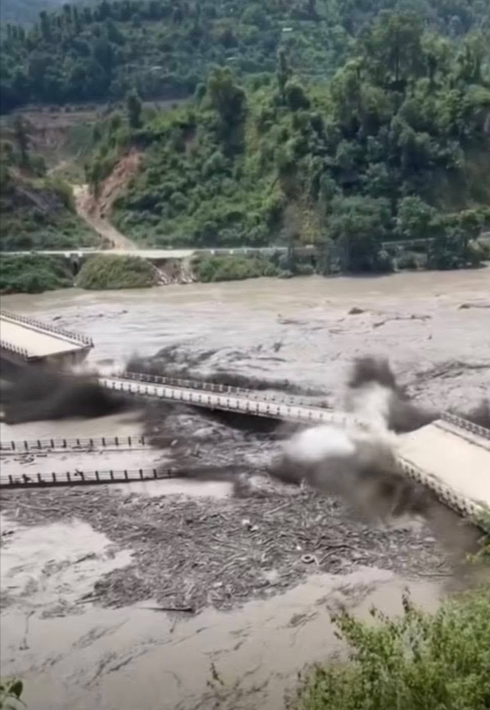 A concrete road bridge collapsing into the swollen, debris-filled river
