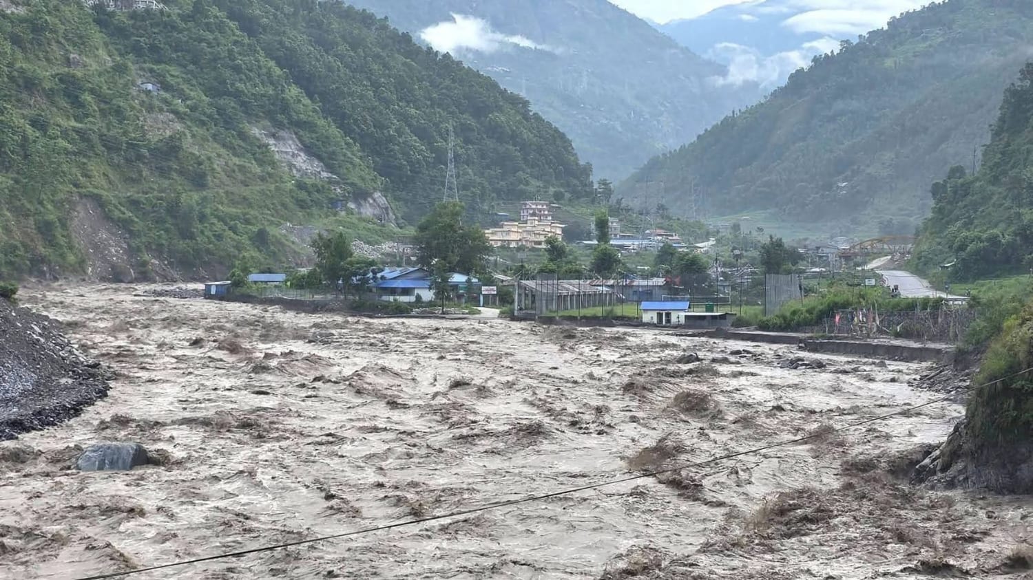 The swollen river cutting through a green Himalayan valley beside a village